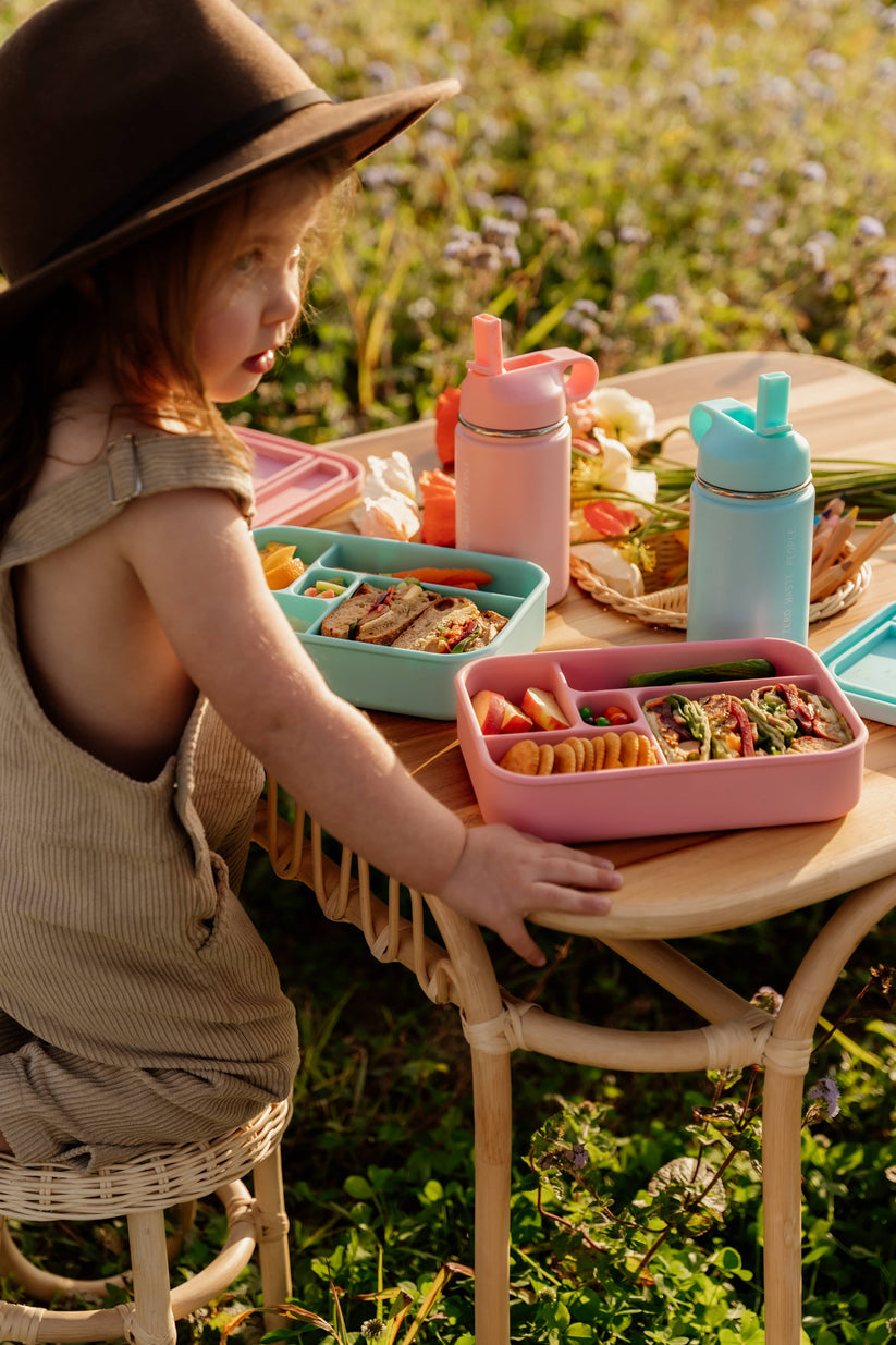 Toddler sitting at a table using Bento Lunchboxes and water bottles from The Zero Waste People