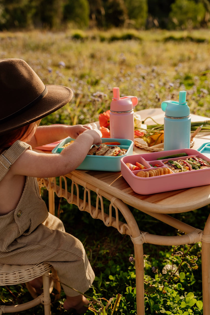 Toddler sitting at a table with bento lunchboxes and water bottles from The Zero Waste People